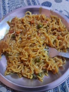 a plate full of noodles and vegetables with a spoon on the side, ready to be eaten