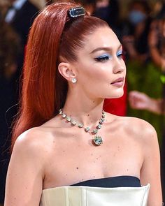 a woman with long red hair wearing a white dress and blue eyeshadow is standing in front of a crowd