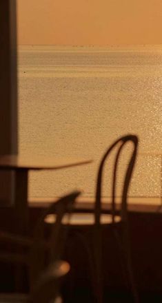 the sun is setting over the ocean with chairs and tables