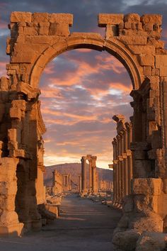 an arch in the middle of a road surrounded by ruins