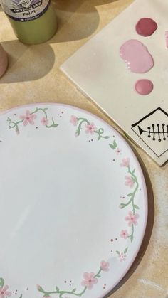 a white plate with pink flowers on it next to other plates and paintbrushes