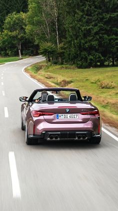 a pink sports car driving down the road with trees in the background and grass on both sides