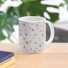 a white and gold coffee mug sitting on top of a wooden table next to a book