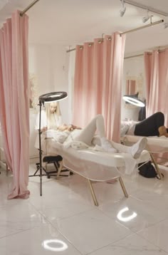 a woman laying on top of a bed in a room with pink curtains and lights
