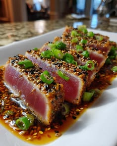 two pieces of meat with sesame seeds and green onions on a white plate sitting on a table