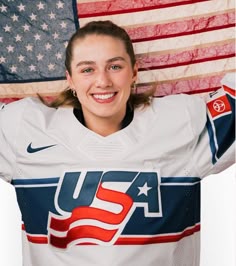 a female hockey player holding an american flag in front of her face and smiling at the camera