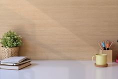 a desk with books, pens and pencils next to a cup on the table
