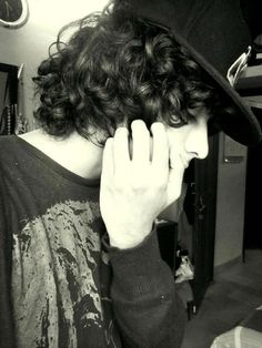 a man with curly hair wearing a hat and holding his hand to his face while standing in front of a mirror