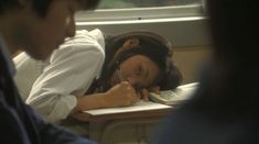 a young woman is writing in her notebook while another man looks on from the other side