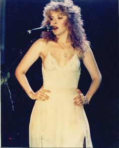 a woman standing in front of a microphone with her hands on her hips while wearing a white dress