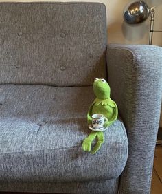a green stuffed animal sitting on top of a couch next to a cup filled with coffee