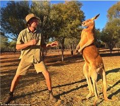 a man standing next to a kangaroo on top of a dry grass field