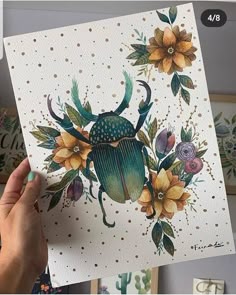 a person holding up a card with an image of a beetle on it and flowers