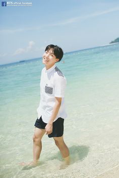 a young man walking on the beach with his feet in the water and smiling at the camera