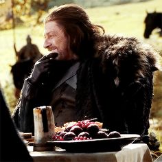 a man sitting at a table in front of a plate with food on it and cows behind him