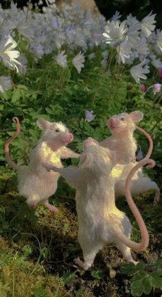 two toy mice playing with each other in the grass near flowers and plants, one has its head on another mouse's back