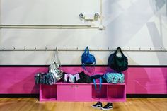 a pink bench with bags and purses on it in front of a white wall