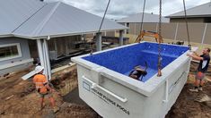 two men working on a construction project in front of a house with a blue swimming pool