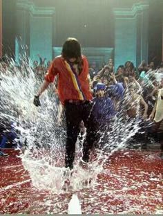 a man in an orange shirt splashes water on his face as people look on