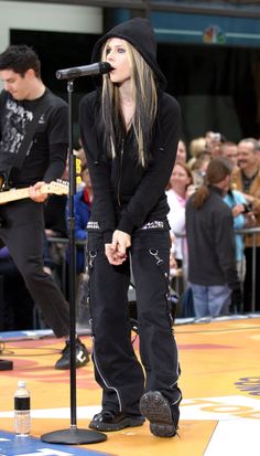 a woman standing in front of a microphone on top of a stage with other people watching