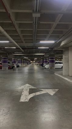 an empty parking garage with several cars parked in the space and one arrow painted on the floor