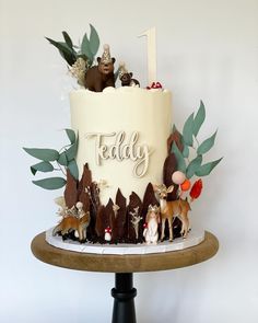 there is a cake decorated with animals and leaves on the top tier, which reads teddy
