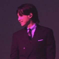 a young man in a suit and tie standing next to a purple light with his hands on his hips