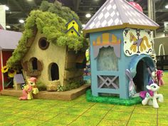 several small toy houses are on display in a building with trees and other toys around them