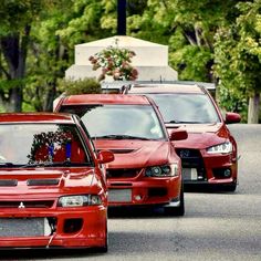 three red cars are parked on the side of the road with trees in the background