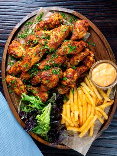 chicken wings, fries and lettuce on a wooden platter with dipping sauce