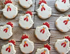 many decorated cookies with red and white icing in the shape of chickens on a wooden surface