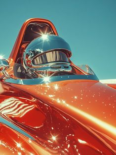 the front end of an orange classic car with its hood up and lights on it