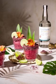 there is a bottle of gin and two cups with flowers in them