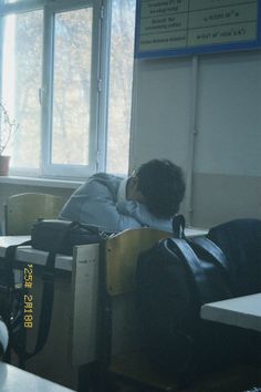 a man sleeping in a classroom with his back to the desk and luggage on it