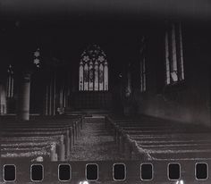 black and white photograph of rows of pews in front of a stained glass window