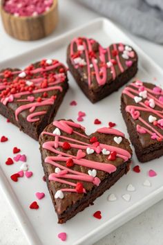 four heart shaped brownies on a plate with sprinkles and pink icing