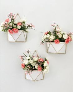 three metal planters with flowers in them hanging on the side of a white wall