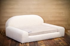 a white dog bed sitting on top of a wooden floor next to a brown wall