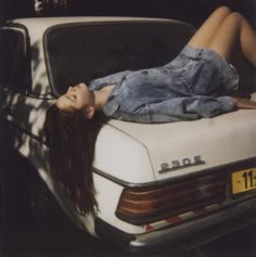 a woman laying on the hood of a car with her head resting on the trunk