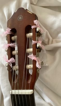 an acoustic guitar with pink flowers on it's back and neck, sitting on a white sheet