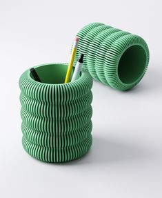 two green cups with pencils in them on a white surface, one is shaped like a spiral