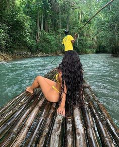 a woman sitting on top of a bamboo raft in the middle of a river surrounded by trees