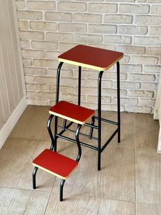 three tiered stools with red seats against a brick wall