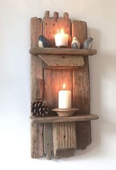 two wooden shelves with candles on them and pine cones in the corner next to each other