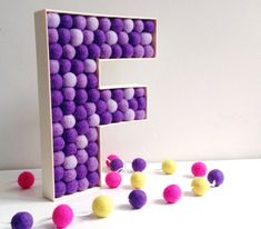 the letter e is made out of felt balls and sits on a table next to some small pom - poms