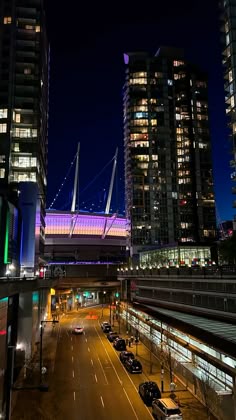a city street at night with cars driving on the road and tall buildings in the background