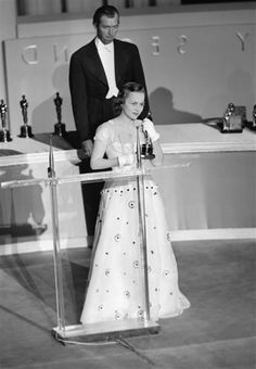 an old photo of a woman standing at a podium in front of a man wearing a tuxedo