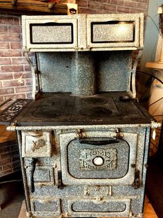 an old fashioned stove sitting on top of a wooden floor next to a brick wall