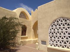 an adobe building with two arched windows and a small tree in the foreground on a sunny day