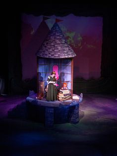 the stage is lit up with purple lighting and an old fashioned doll house on it